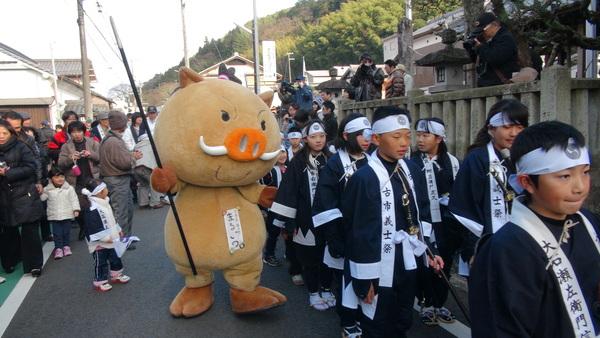 槍を振りかざしているゆるキャラ「まるいの」と一緒に練り歩く子ども義士行列の写真